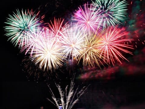 Farbenfrohes Silvesterfeuerwerk über einem Schiff auf dem Wasser
