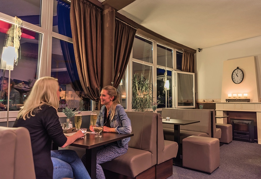 Gäste genießen Getränke in der gemütlichen Bar des Hotel Am Wall mit Kamin und stilvollem Ambiente
